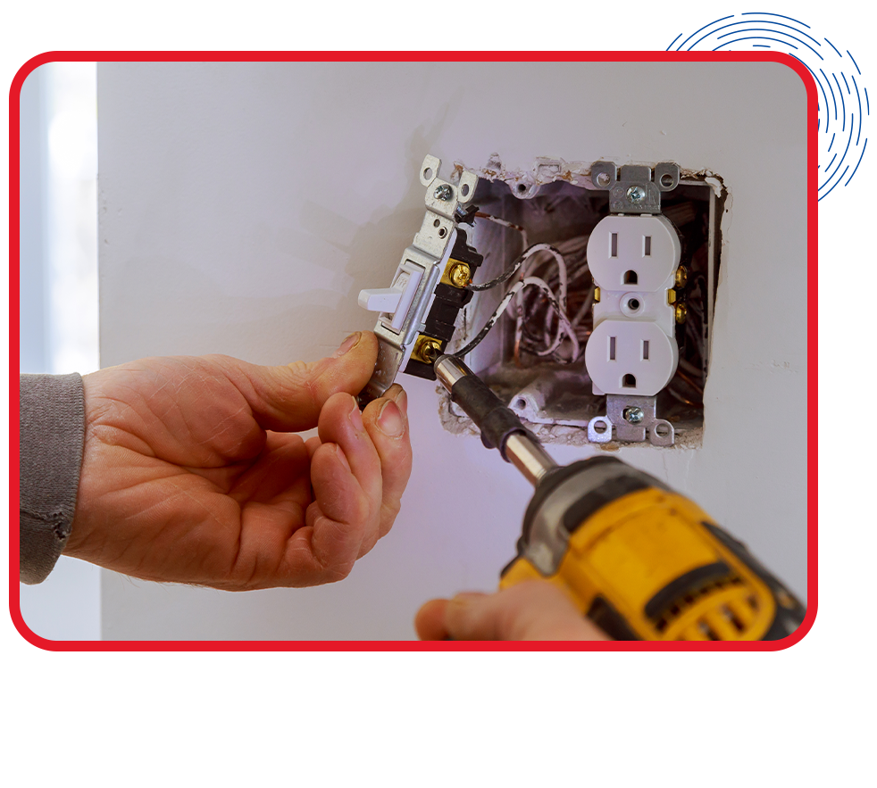 A person installs a light switch plate using a screwdriver next to a double electrical outlet on a white wall. Focus on hands and tools.