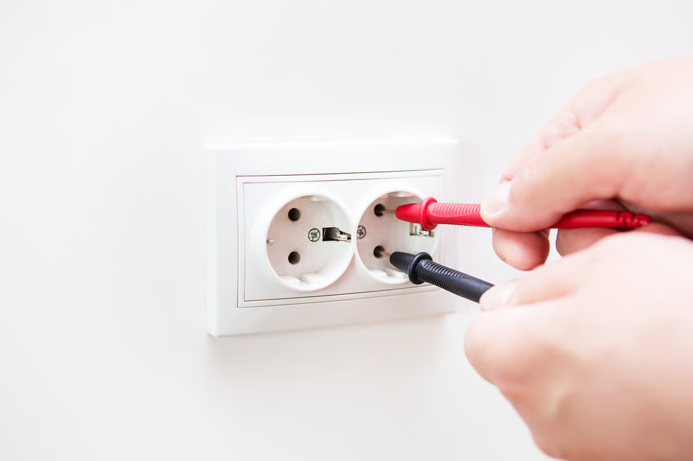 An electrician uses testing tools during electrical services to check a wall outlet.